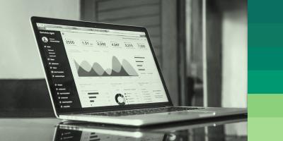 A laptop displaying an analytics and monitoring tool on the screen. Several charts and graphs are visible, including a line chart and a pie chart showing user data. The background features various shades of green.