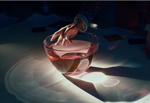 Kuvituskuva, Kädessä pidetty lasimalja heijastuu pöydälle.