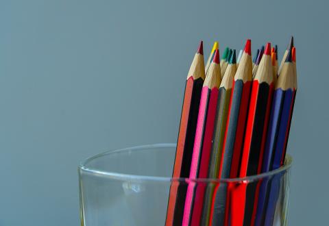 Ett glas med färgpennor i olika färger mot en grå bakgrund.